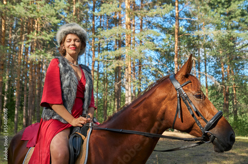 Woman in traditionsl clothes rides a horse in summer forest