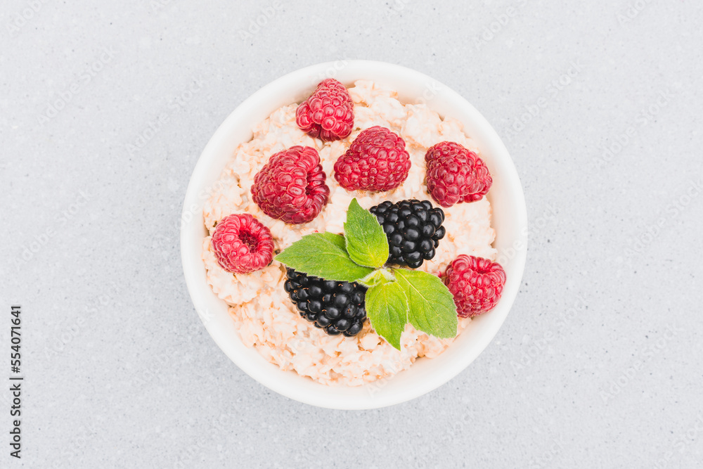 Oatmeal porridge garnished with berries and mint leaves in white bowl on the table. Morning superfood porridge recipe. Healthy breakfast ideas. View above Oatmeal porridge garnished with berries and mint leaves in white bowl on the table. Morning superfood porridge recipe. Healthy breakfast ideas. View above