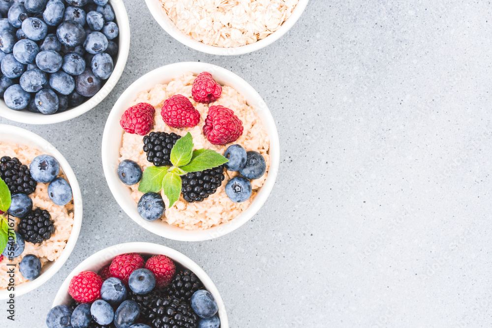 Healthy breakfast - bowls with oatmeal porridge garnished with various berries on concrete table background with copy space. Morning superfood porridge recipe Healthy breakfast - bowls with oatmeal porridge garnished with various berries on concrete table background with copy space. Morning superfood porridge recipe
