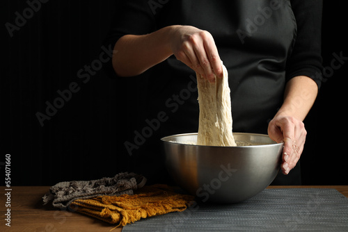 Fotografi The hands of the cook knead the yeast dough in a bowl on a black background