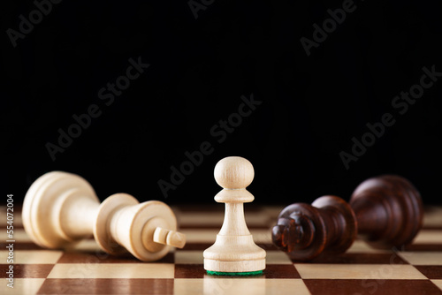 Light chess pawn on a wooden board with lying light and dark chess kings.