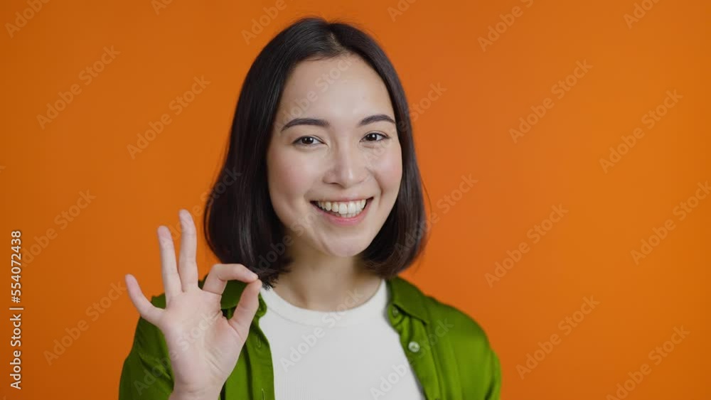 Optimistic Asian woman shows Okay sign and nods approvingly Optimistic Asian woman shows Okay sign and nods approvingly