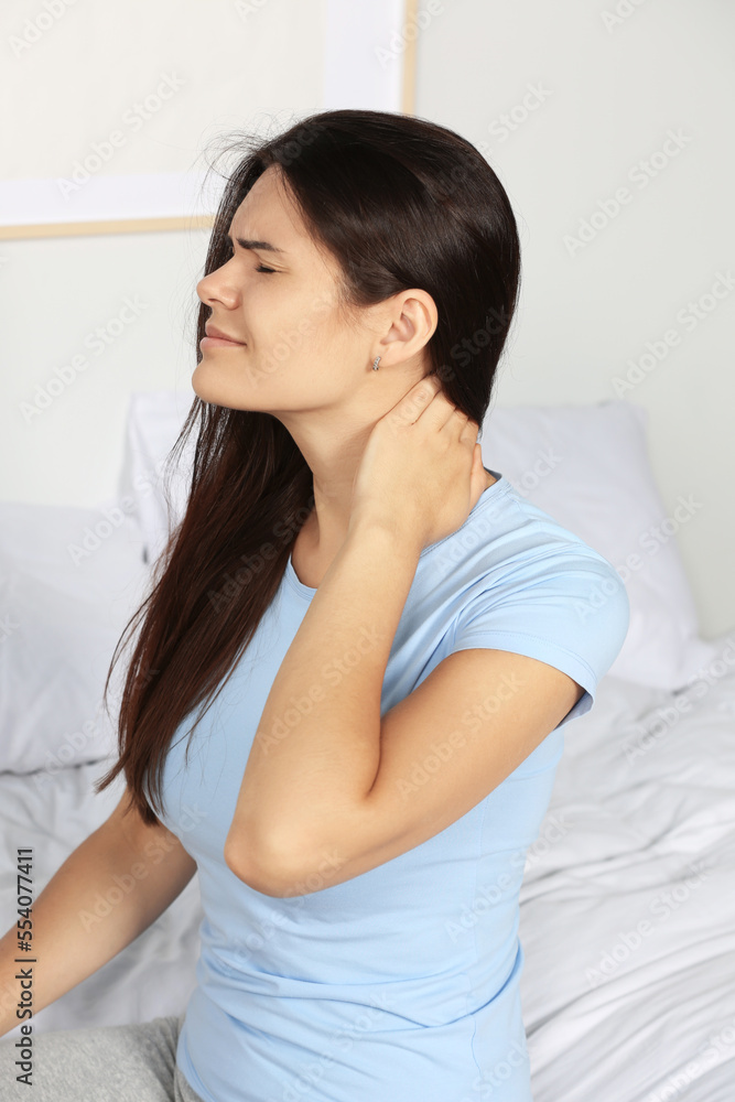 Young woman suffering from neck pain on bed in bedroom Young woman suffering from neck pain on bed in bedroom