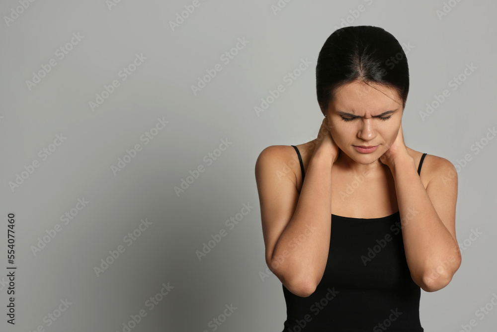 Young woman suffering from neck pain on grey background, space for text Young woman suffering from neck pain on grey background, space for text