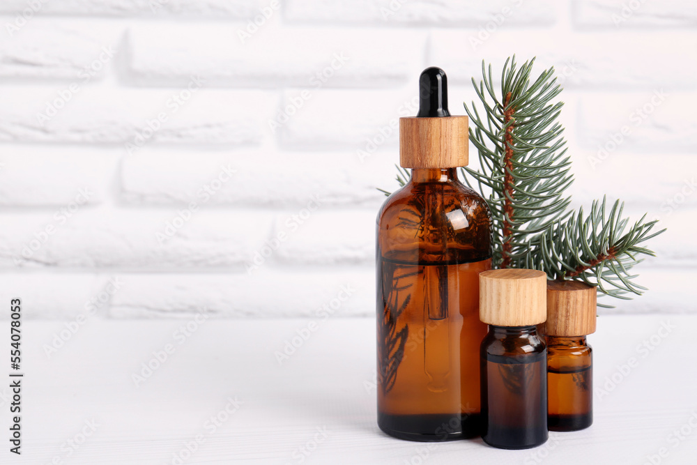Bottles of essential oil and pine branch on white wooden table near brick wall, space for text Bottles of essential oil and pine branch on white wooden table near brick wall, space for text