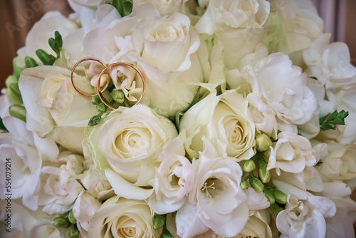 The bride's bouquet consists of white roses and pink hydrangeas, wedding rings on the bouquet. Close-up.