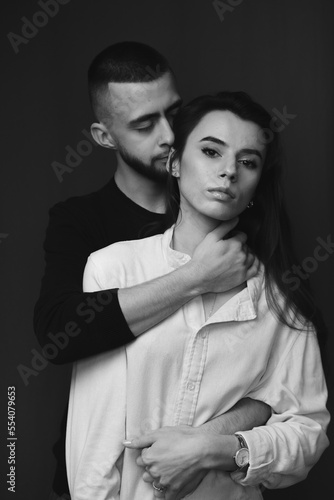 the guy is gently hugging his girlfriend from behind. black and white