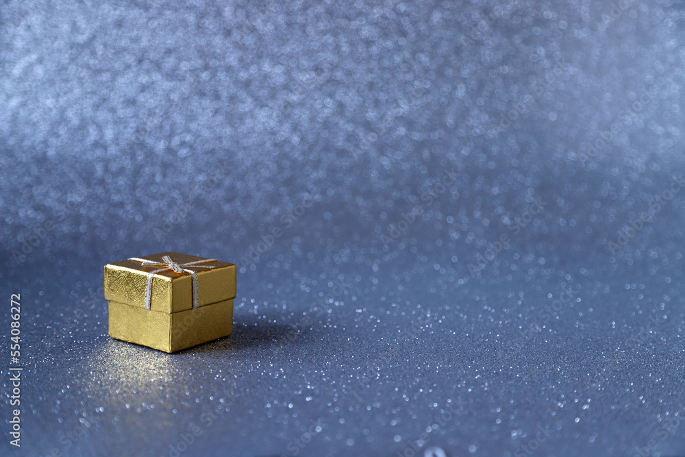 Golden gift box on blue sparkling glittery background. Photo with selective focus. Backdrop with copy space