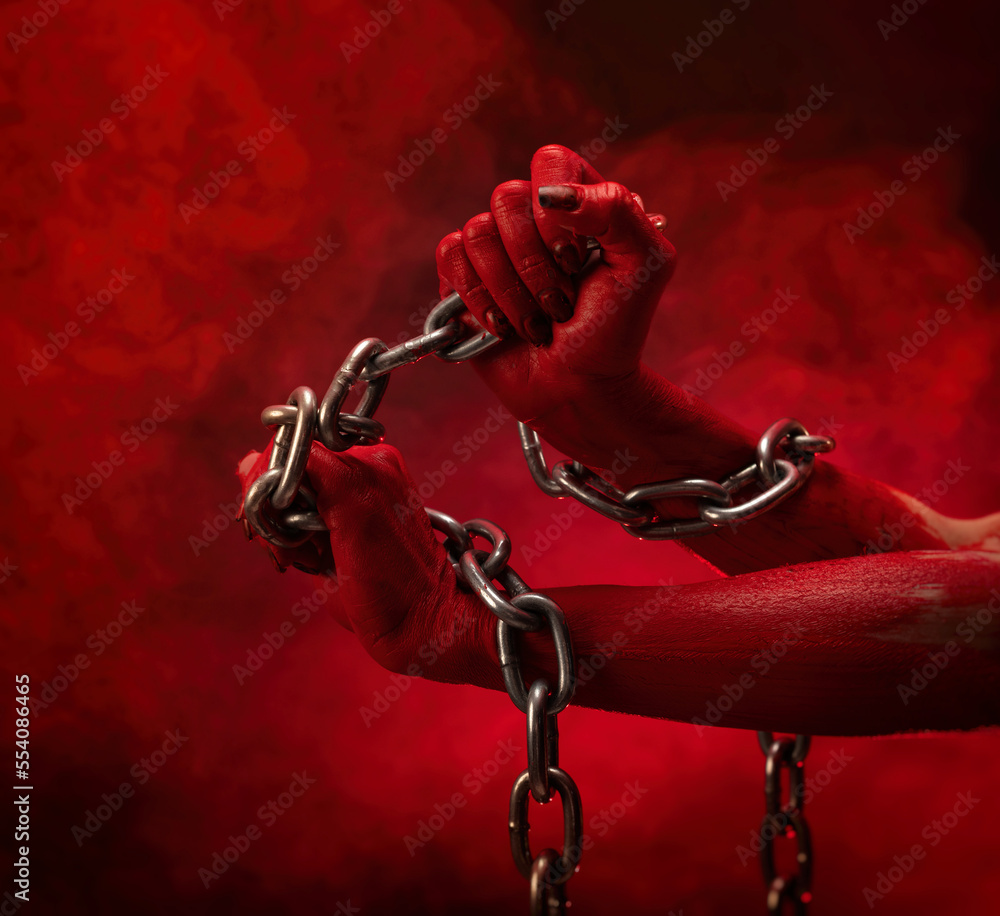 bloody hands clenched into fists in the shackles of a metal chain