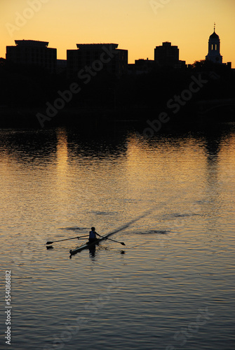 A lone rower plies the waters of the Charles River near Harvard University in Cambridge - Boston during sunrise and is rendered into silhouette photo