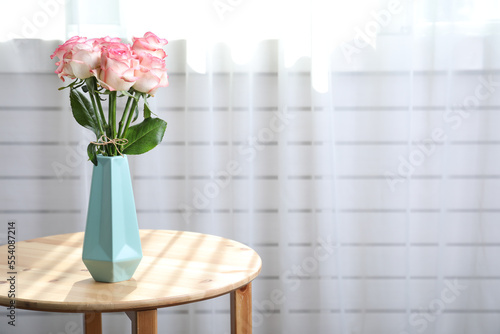 Vase with beautiful pink roses on wooden table in room. Space for text
