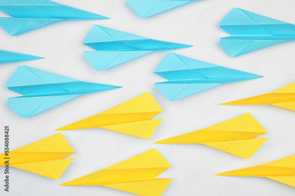 Handmade paper planes in light blue and yellow colors on white table, flat lay