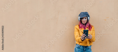 urban style girl with mobile phone and earphones isolated on the wall in the street outdoors © carballo