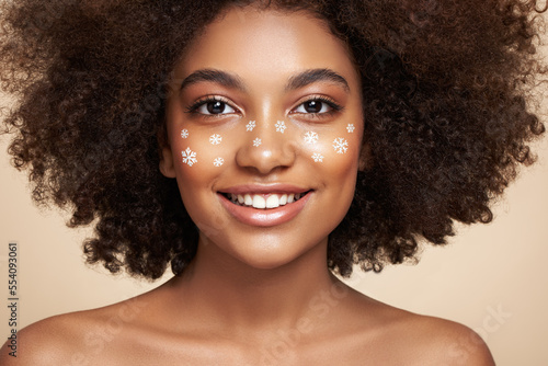 Beauty portrait of African girl with snowflakes her face. Beautiful black woman. Cosmetics, makeup and fashion. Beauty model with curly afro hair. Christmas or New Year festivities makeup