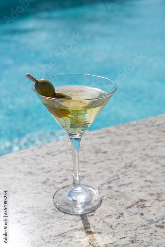 Bild auf Leinwand COLD MARTINI GLASS WITH OLIVES ON THE SHORES OF A POOL ON A SUNNY DAY