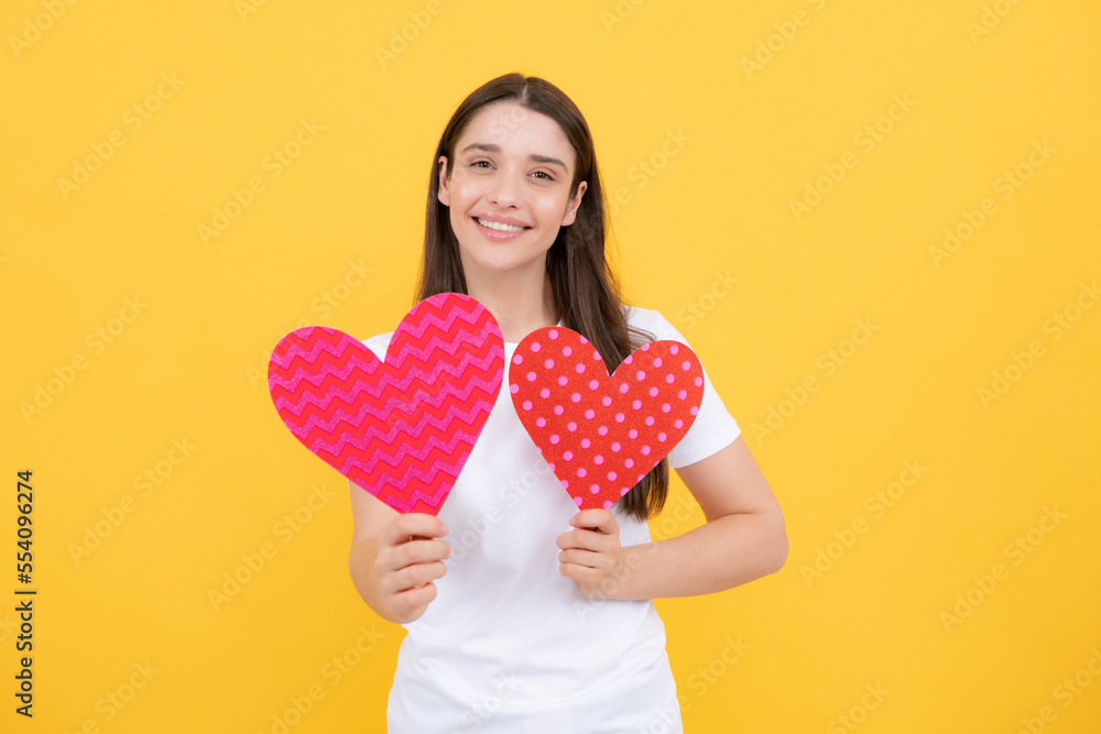 Young woman valentines day concept, girl with heart shaped card. Lovely charming girl holding in hands heart love symbol isolated on yellow background. Young woman valentines day concept, girl with heart shaped card. Lovely charming girl holding in hands heart love symbol isolated on yellow background.