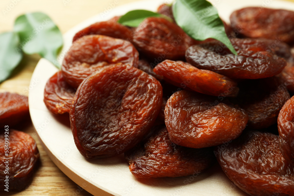 Plate of tasty apricots and green leaves on wooden table, closeup. Dried fruits Plate of tasty apricots and green leaves on wooden table, closeup. Dried fruits