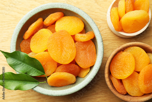 Tasty apricots with green leaves on wooden table, flat lay. Dried fruits
