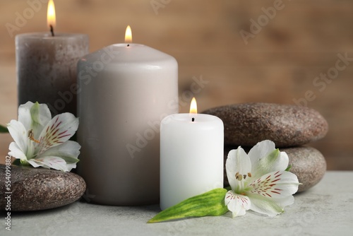 Beautiful composition with burning candles  spa stones and flowers on light grey table  closeup