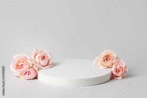 Empty wide white podium and pink roses on light grey background. Minimal cosmetic template. Round showcase for product marketing. Abstract display or stage. Spa and beauty concept. Still life.