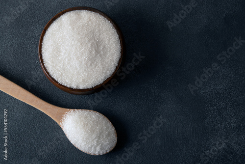 Granulated sugar in bowl on dark background,top view