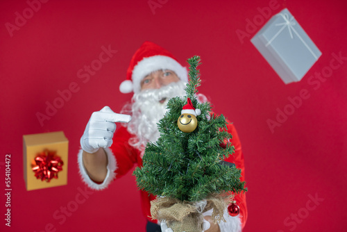 Wallpaper Mural Portrait von einem verkleideten Weihnachtsmann mit Geschenk und Weihnachtsbaum, isoliert auf roten Hintergrund im Studio 
 Torontodigital.ca