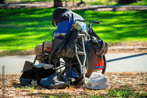 Wheelchair with bags and belogings from a homeless man or woman sitting in a park on the dirt with background grass