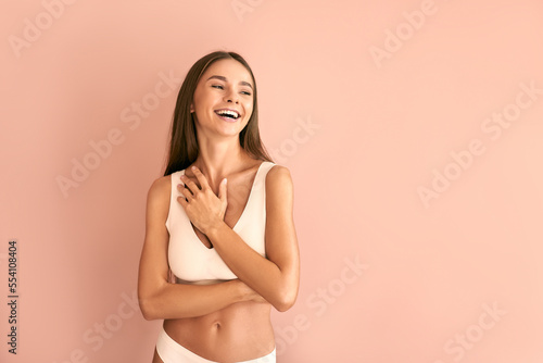  Attractive young woman in white basic underwear laughing on pink background.
