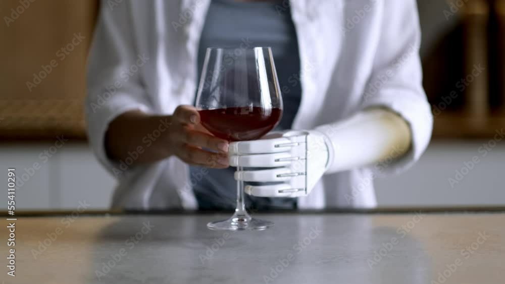 Happy girl with prosthetic arm holds glass of wine in artificial prosthetic limb hand at home Happy girl with prosthetic arm holds glass of wine in artificial prosthetic limb hand at home