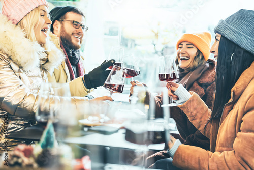 Young people toasting red wine at restaurant pub - Happy friends having fun together at winery bar wearing winter clothes - Dining lifestyle and friendship  concept - Focus on  central glass