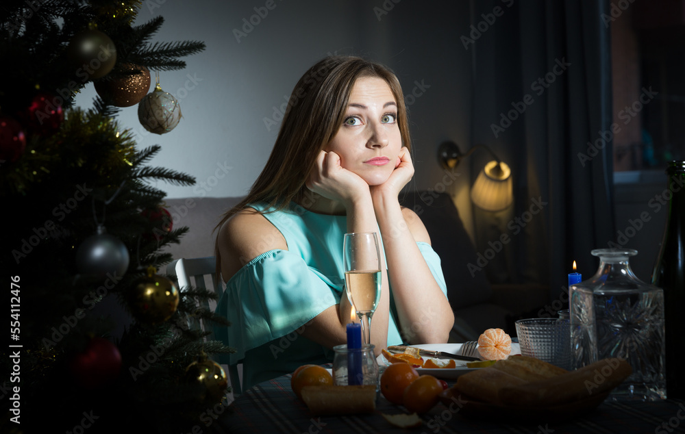Sad woman celebrating Christmas at home alone, sitting at festive table