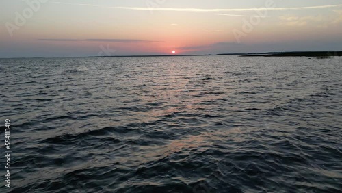 Flying low over an ocean, sea or water as the sun sets on the horizon. Small waves on sea. Sunny sunset over the sea. Aerial view of drone flight over the water revealing the sunset