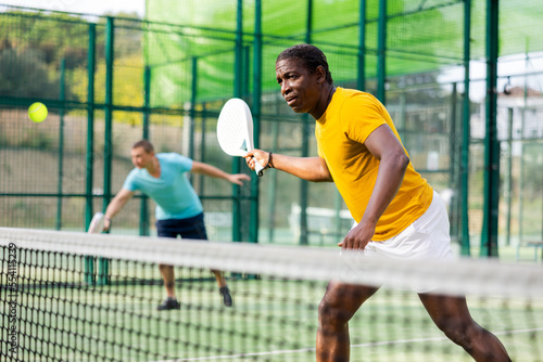 African-american male padel tennis player training on court. Man using racket to hit ball. © JackF