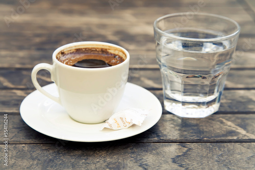 Small cap of strong coffee espresso with glass of clean water on wooden table.
