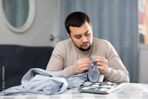 Man sewing button on a shirt sleeve at home