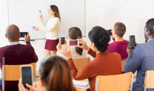 .Female teacher standing in front of whiteboard and people shooting on smartphones her