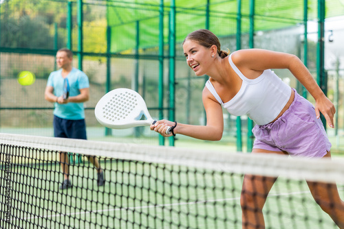 Caucasian young woman in tank top and shorts playing padel tennis match during training on court. © JackF