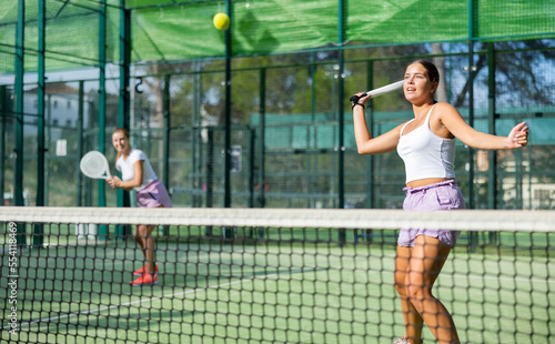 Two active women tennis players, playing padel on an outdoor court, using rackets to hit the ball