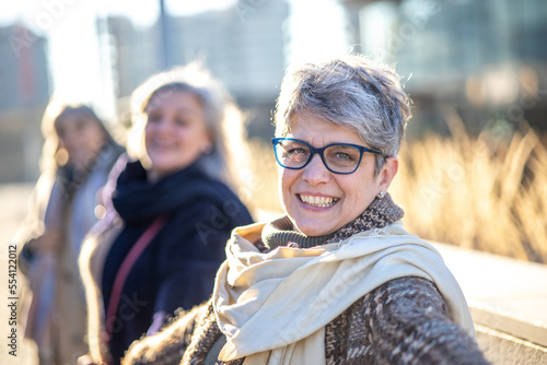 Canvastavla Smiling mature woman holding hands with her group of female friends outside
