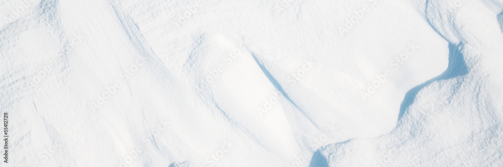 Obraz premium Wide panoramic winter background with snowy ground. Natural snow texture. Wind sculpted patterns on snow surface.