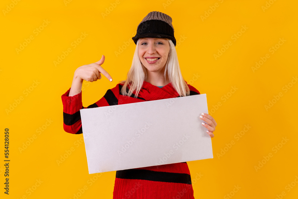 Smiling pointing to an empty ad poster, blonde caucasian girl on yellow background studio Smiling pointing to an empty ad poster, blonde caucasian girl on yellow background studio