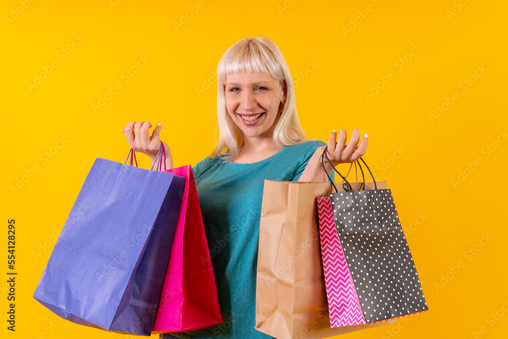 smiling shopping with bags on sale, blonde caucasian girl in studio on yellow background