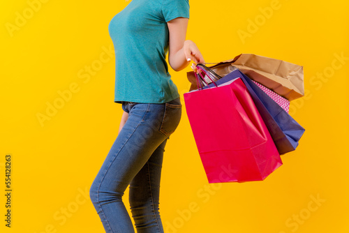 Unrecognizable person with colored shopping bags on discounts, yellow background studio