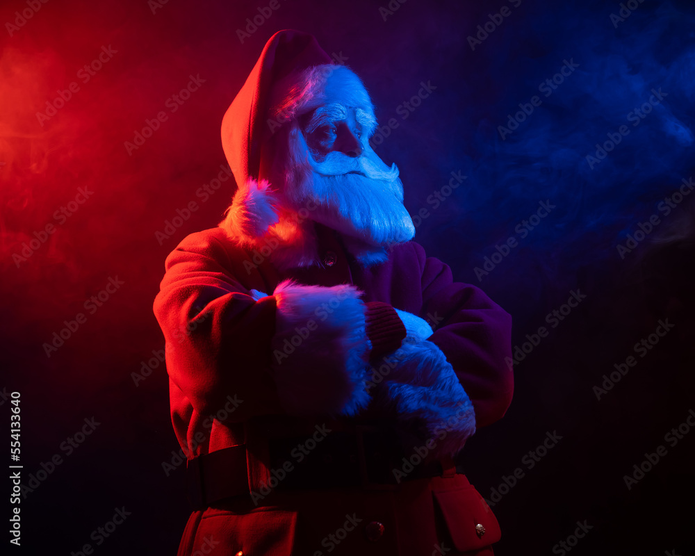 Santa Claus stands with his arms crossed on his chest in blue red neon light and smoke. Santa Claus stands with his arms crossed on his chest in blue red neon light and smoke.