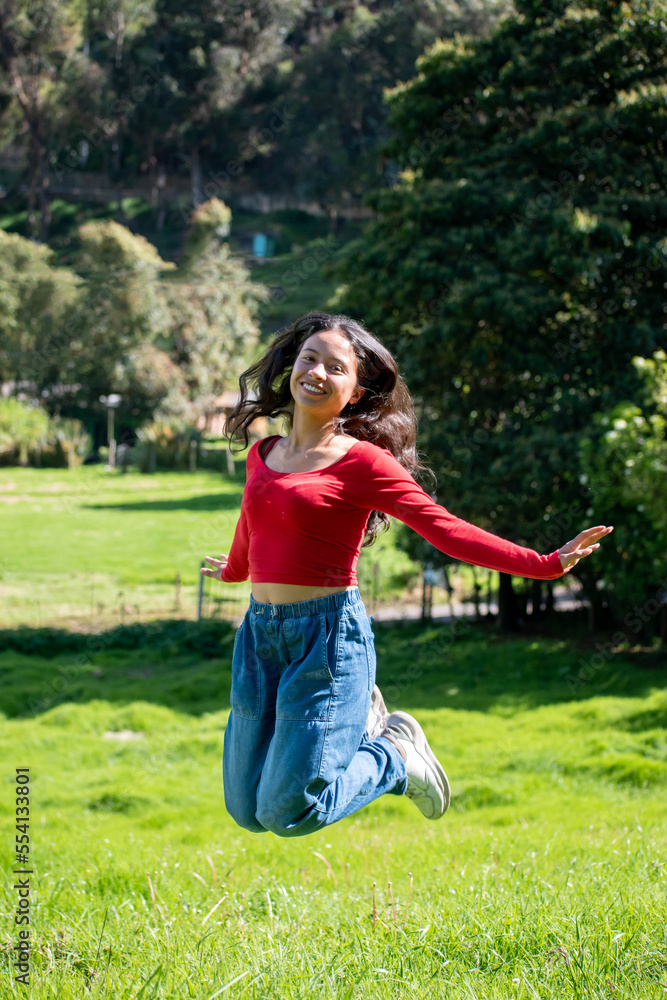 Fototapeta premium young woman jumping happily looking at the camera against a nature background