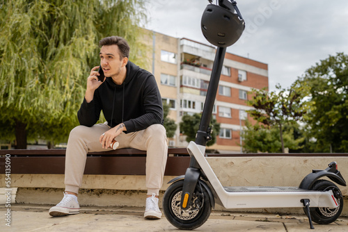 one man sitting on the bench in town with electric kick scooter photo