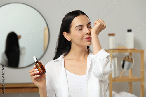 Young woman smelling essential oil on wrist indoors photo