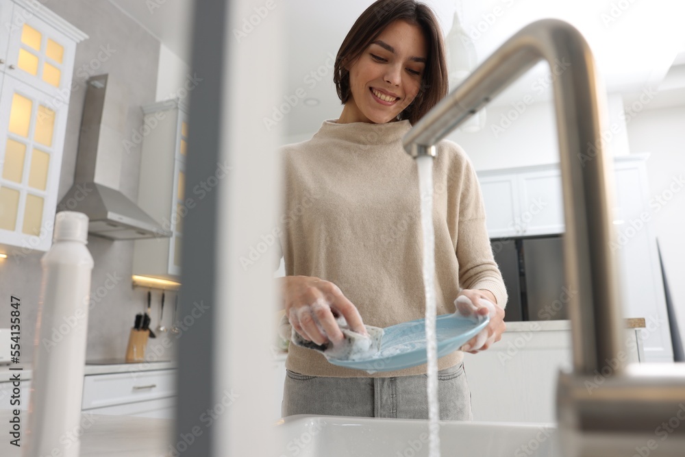 Happy woman washing plate above sink in modern kitchen, low angle view Happy woman washing plate above sink in modern kitchen, low angle view