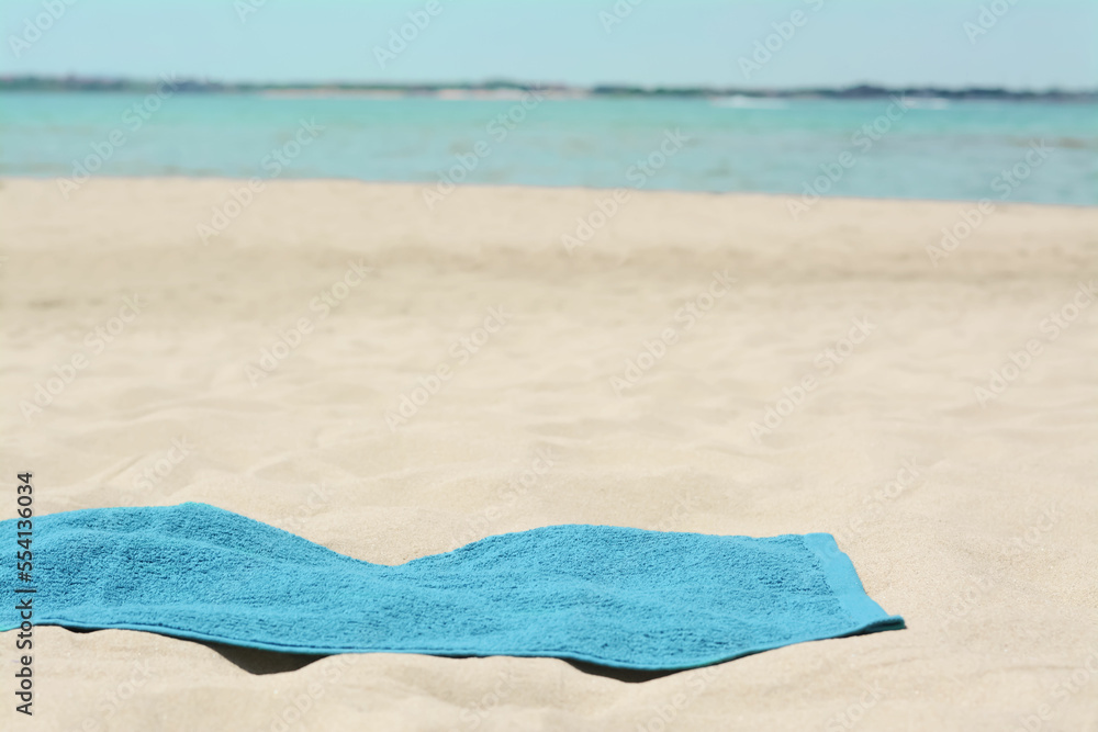Obraz premium Blue towel on sandy beach near sea, space for text