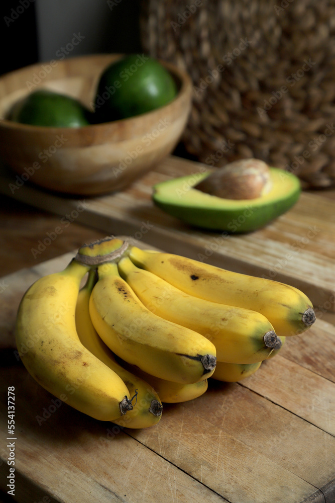 Tropical fruits, delicious bunch of bananas on a wooden table with avocado as a background